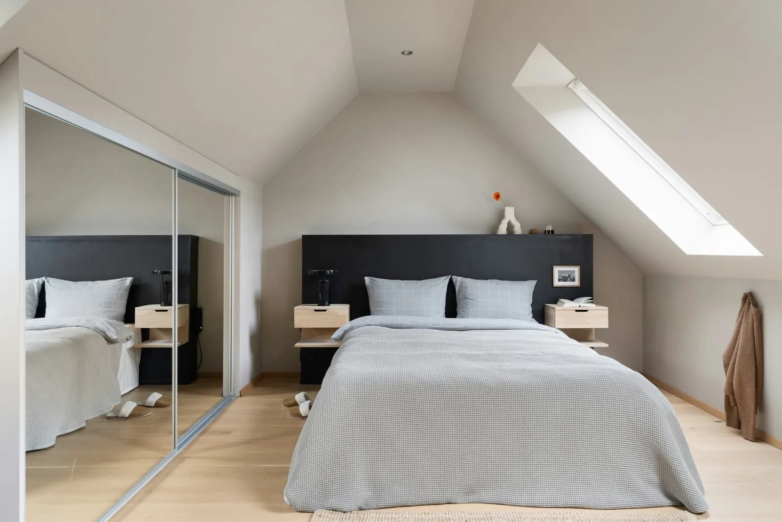 A loft bedroom with a roof window and fitted mirrored wardrobes